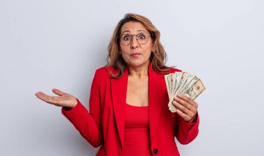Oldukça orta yaşlı bir kadın şaşkın, şaşkın ve şüpheci hissediyor. Dolar banknotları konsepti