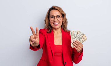 Gülümseyen ve mutlu görünen orta yaşlı bir kadın zafer ya da barış işareti yapıyor. Dolar banknotları konsepti