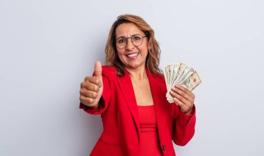 Güzel, orta yaşlı bir kadın gururlu, olumlu gülümsüyor. Dolar banknotları konsepti