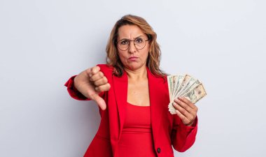Orta yaşlı güzel bir kadın, kendini kötü hissediyor, baş parmağını kaldırıyor. Dolar banknotları konsepti