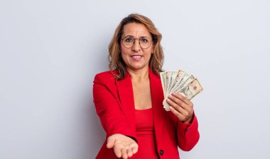 Sevimli orta yaşlı bir kadın arkadaşça gülümsüyor ve bir konsept sunuyor. Dolar banknotları konsepti