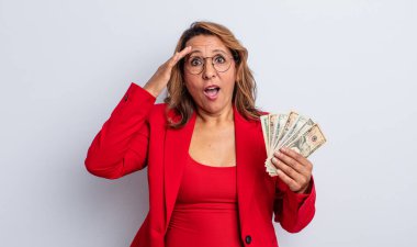 Oldukça orta yaşlı bir kadın mutlu, şaşkın ve şaşırmış görünüyor. Dolar banknotları konsepti
