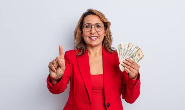 Gülümseyen ve arkadaş canlısı görünen orta yaşlı bir kadın. Bir numarayı gösteriyor. Dolar banknotları konsepti