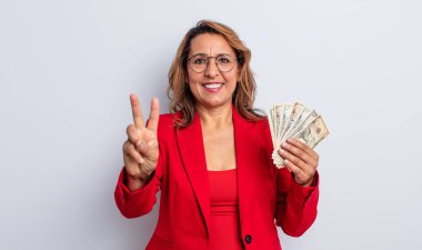 Gülümseyen ve arkadaş canlısı görünen orta yaşlı bir kadın. İki numarayı gösteriyor. Dolar banknotları konsepti