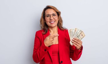 Sevimli orta yaşlı bir kadın neşeli bir şekilde gülümsüyor, mutlu hissediyor ve bir tarafı işaret ediyor. Dolar banknotları konsepti