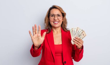 Güzel orta yaşlı bir kadın gülümsüyor ve arkadaş canlısı görünüyor, beş numarayı gösteriyor. Dolar banknotları konsepti