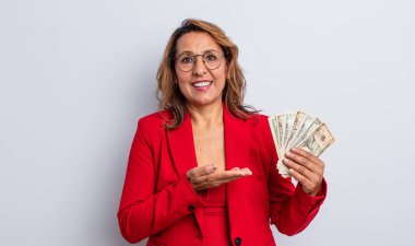 Sevimli orta yaşlı bir kadın neşeli bir şekilde gülümsüyor, mutlu hissediyor ve bir konsept gösteriyor. Dolar banknotları konsepti