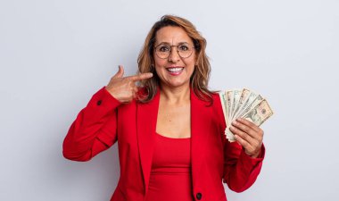 Güzel, orta yaşlı bir kadın kendi gülüşünü işaret ederek gülümsüyor. Dolar banknotları konsepti