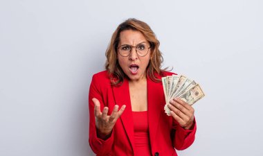 Oldukça orta yaşlı bir kadın sinirli, sinirli ve hayal kırıklığına uğramış görünüyor. Dolar banknotları konsepti