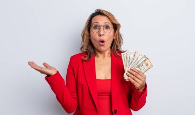 Oldukça orta yaşlı bir kadın şaşırmış ve şok olmuş görünüyor. Çenesi düşmüş ve elinde bir nesne var. Dolar banknotları konsepti