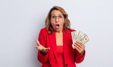 Oldukça orta yaşlı bir kadın son derece şaşırmış ve şok olmuş hissediyor. Dolar banknotları konsepti
