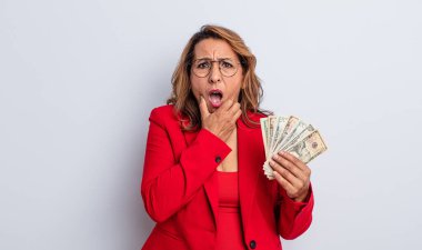 Ağzı ve gözleri açık, elleri çenesinde, orta yaşlı güzel bir kadın. Dolar banknotları konsepti
