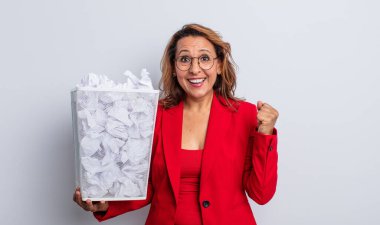 Oldukça orta yaşlı bir kadın şokta, gülüyor ve başarıyı kutluyor. kağıt topları çöp kutusu konsepti