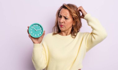 Kafası karışmış, kafası karışmış, kaşınan orta yaşlı bir kadın. Alarm saati kavramı