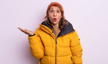 Oldukça orta yaşlı bir kadın şaşırmış ve şok olmuş görünüyor. Çenesi düşmüş ve elinde bir nesne var. kış konsepti