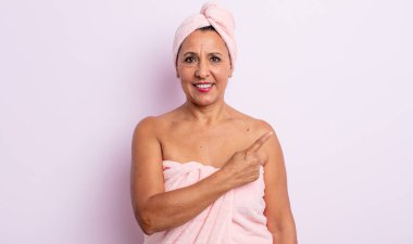 Sevimli orta yaşlı bir kadın neşeli bir şekilde gülümsüyor, mutlu hissediyor ve bir tarafı işaret ediyor. güzellik ve duş konsepti