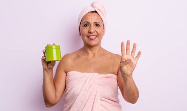 Güzel orta yaşlı kadın gülümsüyor ve arkadaş canlısı görünüyor, dört numarayı gösteriyor. duş ve saç ürünü konsepti