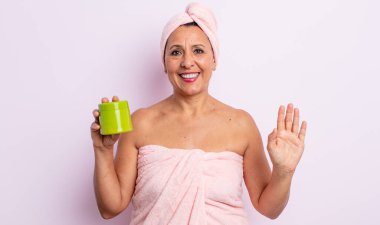 Güzel orta yaşlı bir kadın mutlu bir şekilde gülümsüyor, el sallıyor, sizi selamlıyor ve selamlıyor. duş ve saç ürünü konsepti