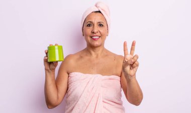 Gülümseyen ve arkadaş canlısı görünen orta yaşlı bir kadın. İki numarayı gösteriyor. duş ve saç ürünü konsepti