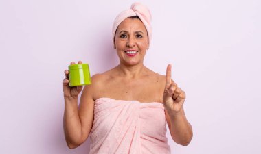 Gülümseyen ve arkadaş canlısı görünen orta yaşlı bir kadın. Bir numarayı gösteriyor. duş ve saç ürünü konsepti