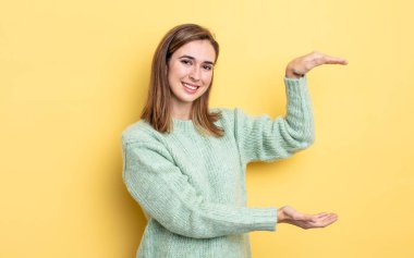 Genç güzel kız gülümsüyor, mutlu, pozitif ve tatmin olmuş hissediyor, fotokopi alanında nesne ya da konsept tutuyor ya da gösteriyor