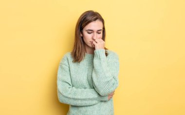 Genç ve güzel bir kız ciddi, düşünceli ve endişeli, elleri çenesine bastırılmış bir şekilde yan bakıyor.