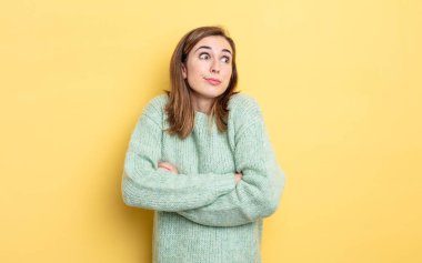 Genç, güzel bir kız omuz silkiyor, kafası karışık ve kararsız, kolları bağlı ve şaşkın görünüyor.