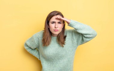 Genç ve güzel kız şaşkınlık ve şaşkınlık içinde bakıyor, el üstünde, uzaklara bakıyor, izliyor ya da arıyor.