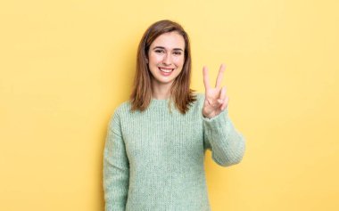 Genç, güzel bir kız gülümsüyor ve arkadaş canlısı görünüyor. İki ya da iki numarayı gösteriyor. Elleri önde, geri sayıyor.