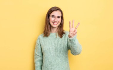 Genç, güzel bir kız gülümsüyor ve arkadaş canlısı görünüyor. Üç ya da üç numarayı gösteriyor. Elleri önde, geri sayıyor.