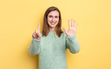 Genç ve güzel bir kız gülümsüyor ve arkadaş canlısı görünüyor, altı ya da altıncı numarayı gösteriyor, elleri önde, geriye doğru sayıyor.