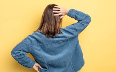 Genç, güzel bir kız bilgisiz ve kafası karışık, bir çözüm düşünüyor, eli kalçasında, diğeri kafasında, dikiz aynasından.