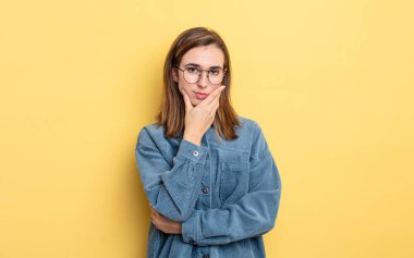 Genç ve güzel bir kız ciddi, düşünceli ve güvensiz görünüyor, bir kolu çapraz ve çene üzerinde, seçenekleri tartıyor.