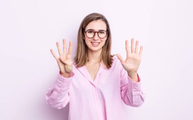 Genç, güzel bir kız gülümsüyor ve arkadaş canlısı görünüyor. 9 ya da 9 numarayı gösteriyor. Elleri önde ve geri sayıyor.