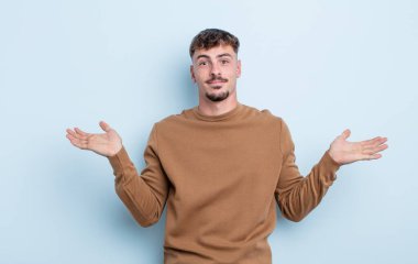 Genç yakışıklı adam şaşkın ve şaşkın, şüpheci, farklı seçenekleri tartıyor ya da komik bir ifadeyle seçiyor.