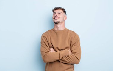 Genç yakışıklı adam mutlu, gururlu ve umutlu, merak ediyor ya da düşünüyor, çapraz kollarla boşluğu dolduruyor.