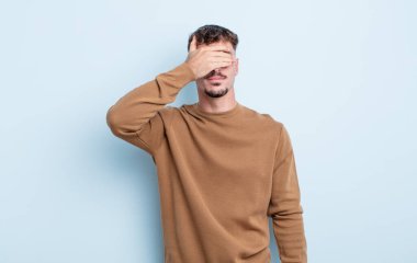 Genç yakışıklı bir adam tek eliyle gözlerini kapatıyor. Korkmuş ya da endişeli, merak ediyor ya da körü körüne bir sürpriz bekliyor.