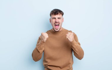 Genç yakışıklı adam sinirli, sinirli, sinirli bakışlar ve sıkı yumruklar ile agresif bir şekilde bağırıyor.