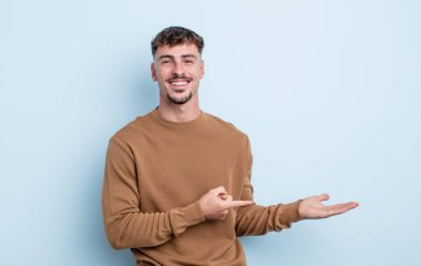 Genç yakışıklı adam gülümsüyor, mutlu, tasasız ve tatmin olmuş hissediyor, fotokopi alanındaki konsepte ya da fikre işaret ediyor.