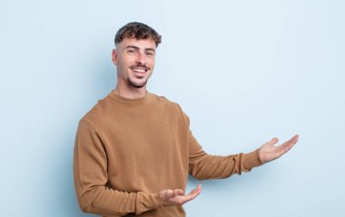 Genç yakışıklı adam gururla ve kendinden emin bir şekilde gülümsüyor, mutlu ve tatmin olmuş hissediyor ve fotokopi alanında bir konsept gösteriyor.