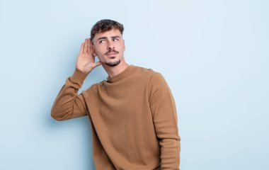 Genç yakışıklı bir adam gülümsüyor, tuhaf bir şekilde yan tarafa bakıyor, dedikoduları dinlemeye ya da bir sırrı duymaya çalışıyor.