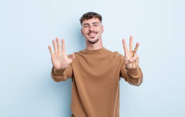 Genç yakışıklı adam gülümsüyor ve arkadaş canlısı görünüyor, 8 ya da 8 numarayı gösteriyor, eli önde, geri sayıyor.