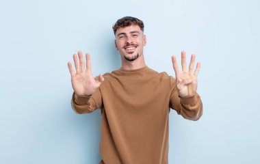 Genç yakışıklı adam gülümsüyor ve arkadaş canlısı görünüyor. 9 ya da 9 numarayı gösteriyor. Elleri önde, geriye doğru sayıyor.