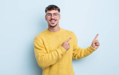 Genç yakışıklı adam mutlu bir şekilde gülümsüyor ve her iki elinde fotokopi alanında nesne gösteriyor.