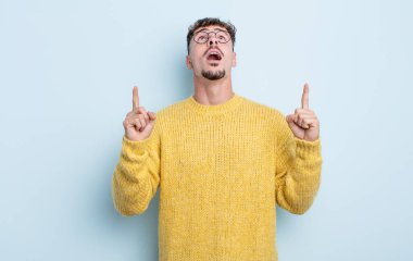 Genç yakışıklı adam şaşırmış, şaşırmış ve ağzı açık, iki eliyle uzayı göstererek