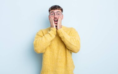 Genç yakışıklı adam şok olmuş ve korkmuş hissediyor, ağzı açık ve elleri yanaklarında korkmuş görünüyor.
