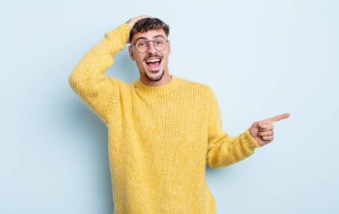 Genç yakışıklı adam gülüyor, mutlu, pozitif ve şaşırmış görünüyor. Yan fotokopi alanını işaret eden harika bir fikrin farkına varıyor.