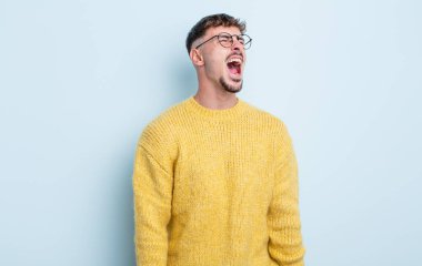 Genç yakışıklı adam öfkeyle bağırıyor, agresif bir şekilde bağırıyor, stresli ve sinirli görünüyor.