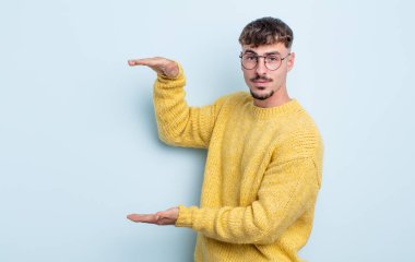 Genç yakışıklı bir adam iki eli de yan tarafında fotokopi alanı olan bir nesneyi tutuyor, bir nesneyi gösteriyor, sunuyor ya da reklamını yapıyor.