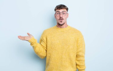 Genç yakışıklı adam şaşırmış ve şoka uğramış görünüyor, çenesi düşmüş, eli açık bir nesneyi tutuyor.